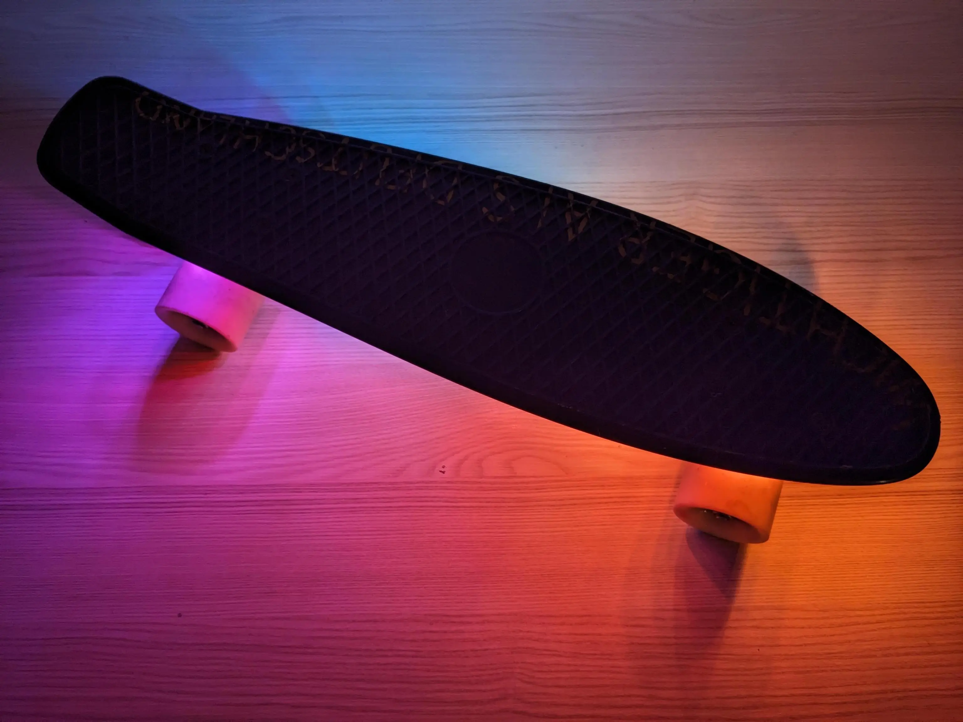 small pennyboard on wooden surface, underside is illuminated by rainbow LED light.